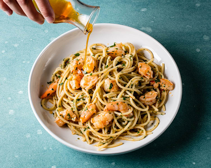 Shrimp Aglio e Olio Pasta with olive oil being poured over the pasta